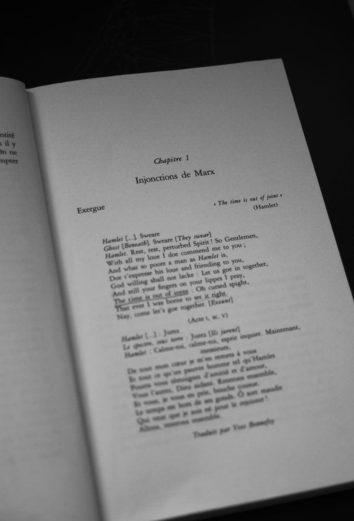 Black-and-white photograph that captures the opening of a book, focusing on Chapter 1, titled Injonctions de Marx (“Injunctions of Marx”). The page features an exergue, or epigraph, drawn from Shakespeare’s Hamlet. At the top right, the quotation “The time is out of joint” is highlighted, followed by excerpts in both English and French. The English passage reproduces part of Hamlet’s dialogue in Act I, Scene V, including the famous lament on time being “out of joint.” Below it, the same lines are translated into French by Yves Bonnefoy, a noted poet and translator.